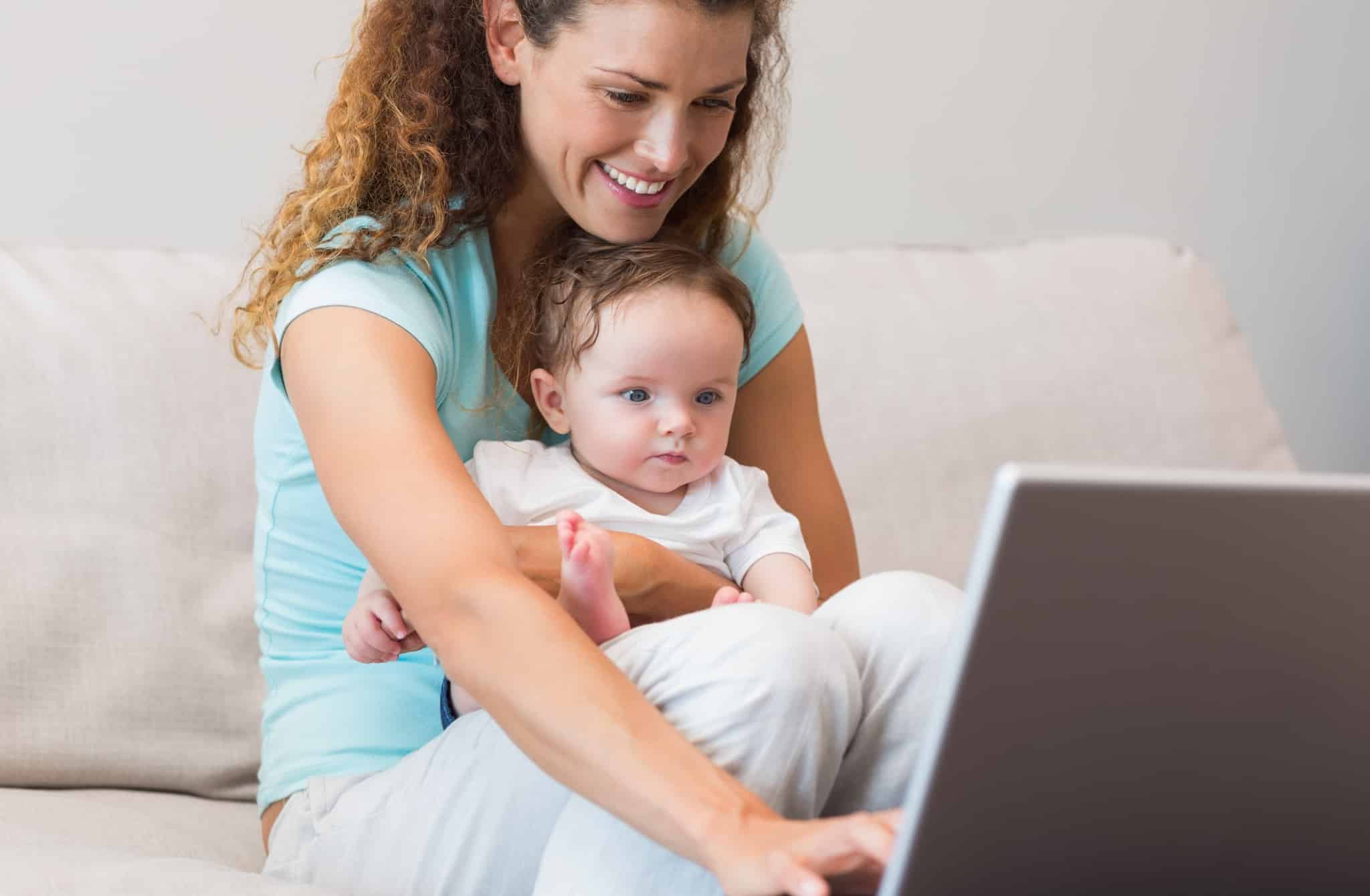 Smiling mother using laptop while holding baby in living room