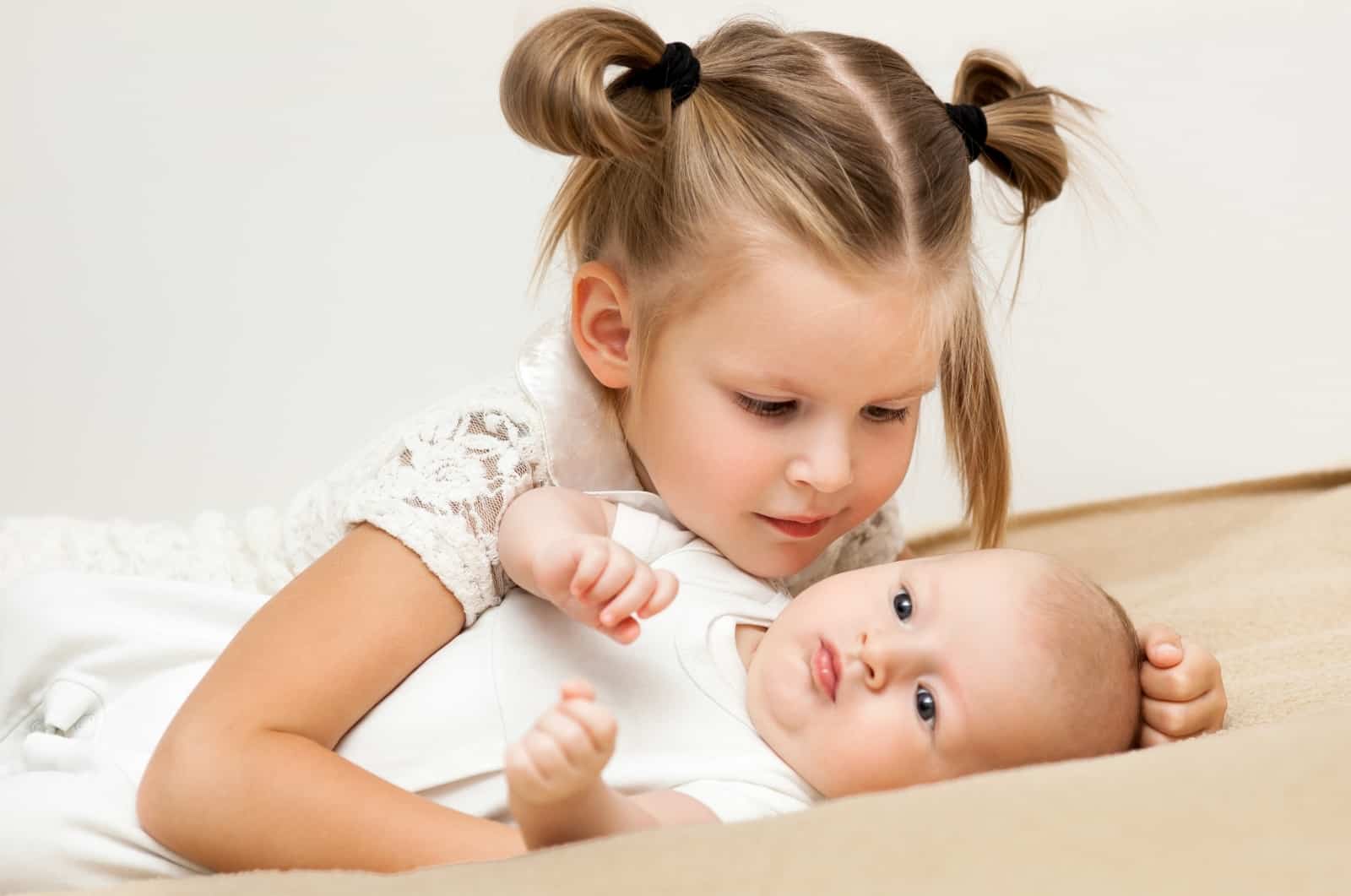 big sister is hugging and talking with her infant little brother with love