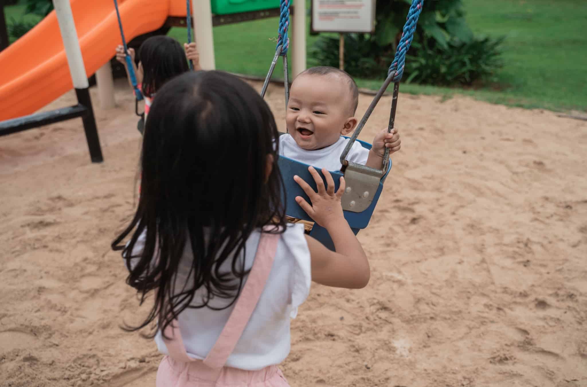 older sibling looking after his baby sister who swings