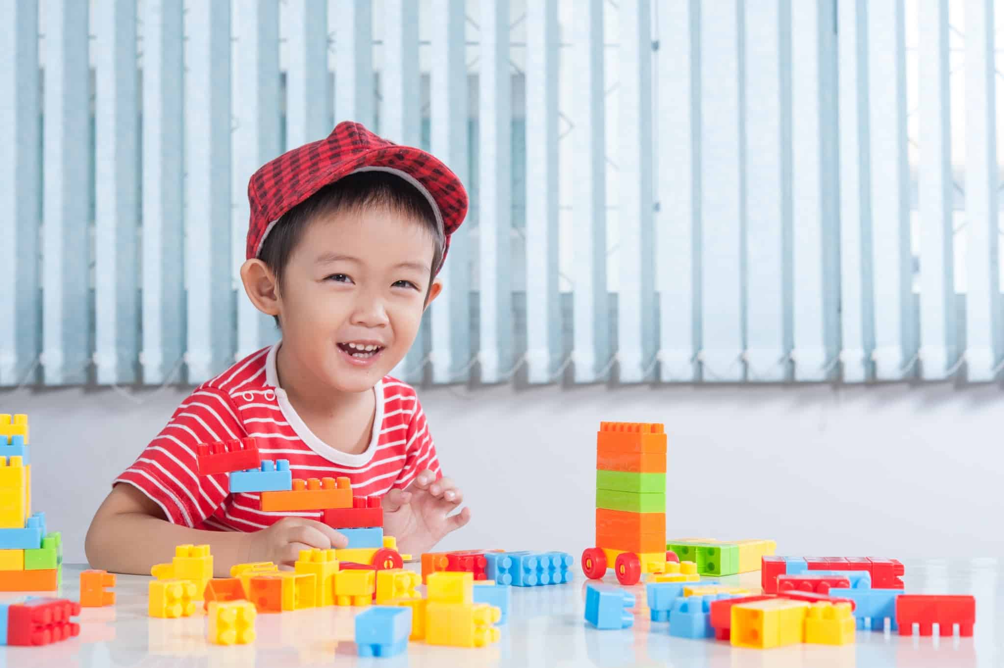 Cute boy playing with colorful plastic bricks at the table in th